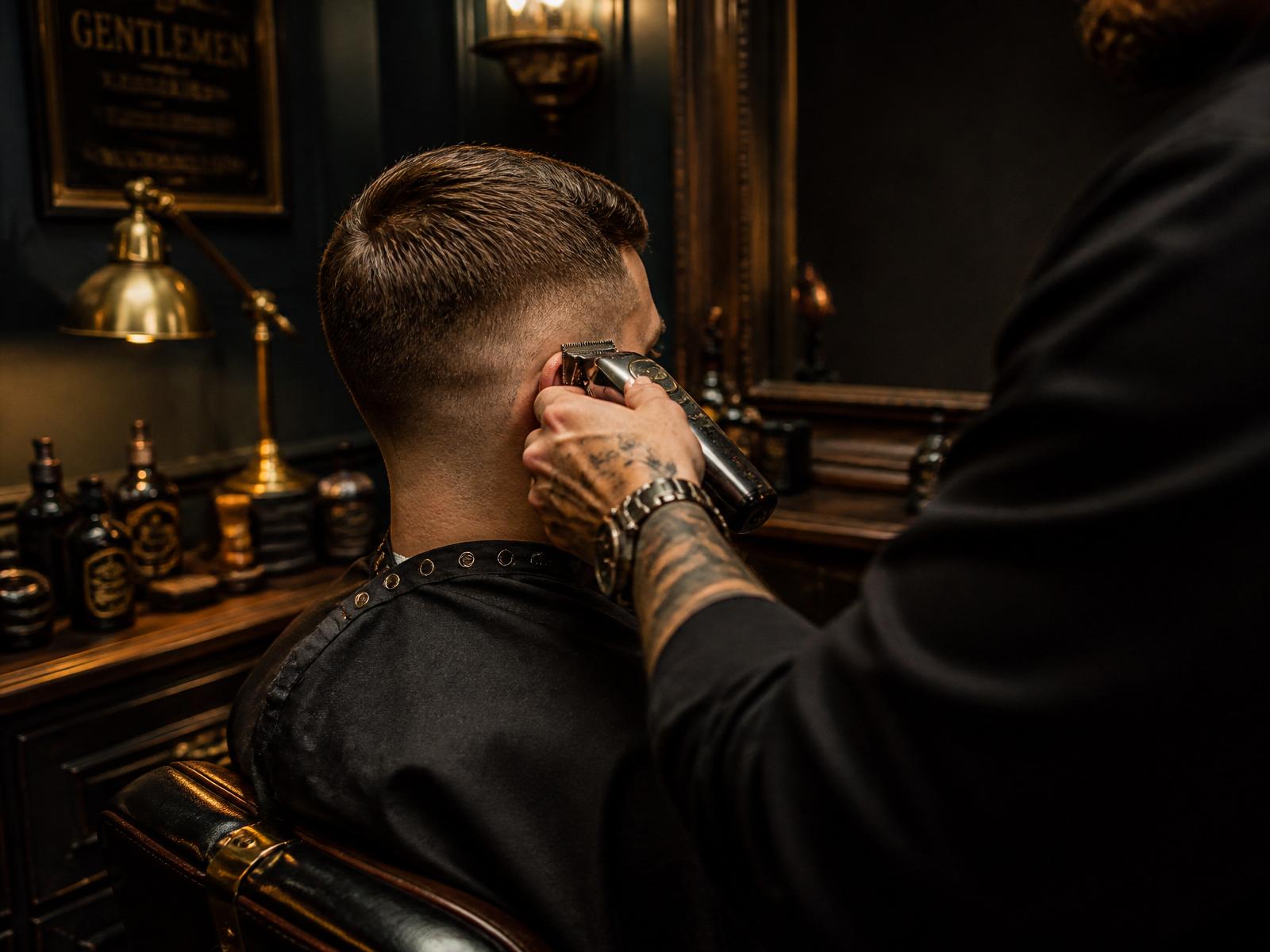Barber wykonujący precyzyjny fade w ciemnym wnętrzu Black Forge Barber